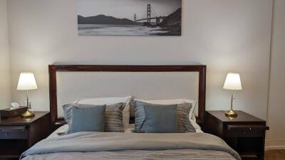 Cozy bedroom with a large bed, matching nightstands and lamps, and a framed picture of a bridge