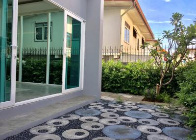 Paved pathway leading to a green house with a cozy front yard