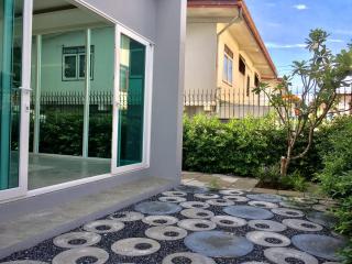 Paved pathway leading to a green house with a cozy front yard