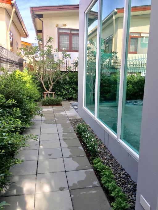 Paved pathway leading to a modern home with a green lawn and large windows