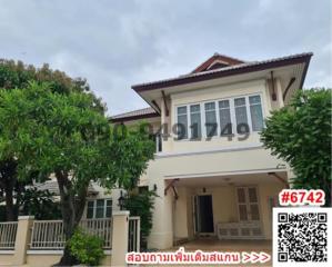 Exterior view of a two-story house with a white facade, surrounded by greenery, under a cloudy sky