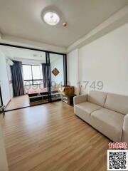 Bright and cozy living room with a beige sofa, wooden flooring, and a large window leading to a balcony