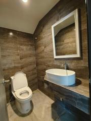 Modern bathroom with dark tile walls, white sink, and toilet