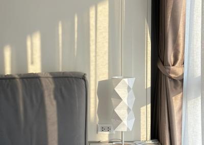 Modern bedroom with sunlight casting shadows on the wall, featuring a stylish bedside lamp and elegant curtains