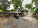 Gravel driveway with a parked car leading to a rural house with trees