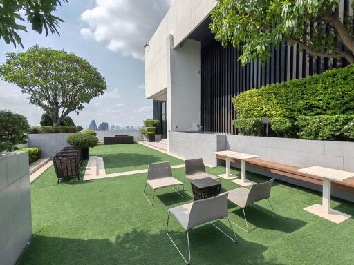 Modern rooftop garden with city skyline view, artificial grass, comfortable seating area, and well-maintained plants