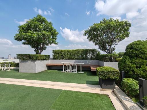 Spacious rooftop garden with seating and greenery under a clear blue sky