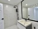 Modern bathroom with white marble walls, frameless mirror, and black fixtures