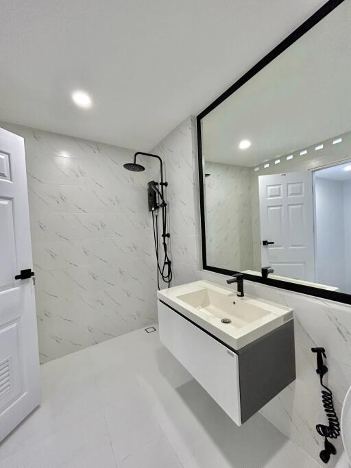 Modern bathroom with white marble walls, frameless mirror, and black fixtures