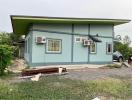 Exterior view of a blue single-story house with a green roof and satellite dish