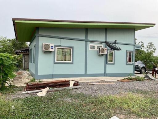 Exterior view of a blue single-story house with a green roof and satellite dish