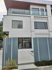 Modern multi-story residential building with glass balcony and front gate