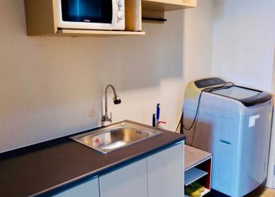 Compact modern kitchen with stainless steel countertop, microwave, and portable washing machine