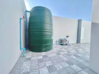 Large green water tank on a tiled outdoor area with pipes and water pump