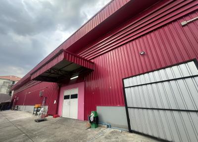 Exterior view of a modern industrial warehouse with red metallic walls and a spacious concrete area