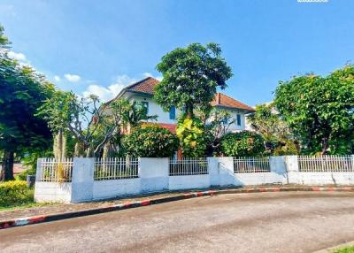 Exterior view of a two-story residential house with a gated fence, surrounded by greenery under a clear sky