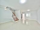 Spacious and bright living area with a modern staircase and glossy floor tiles