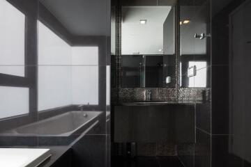 Modern bathroom interior with dark tiles featuring a bathtub and a vanity