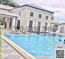 Well-lit exterior view of a two-story house with a swimming pool and garden chairs