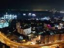 Panoramic night view of a lit modern cityscape with coastal road and buildings
