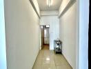 Brightly lit, narrow hallway with beige tiled flooring and a small table