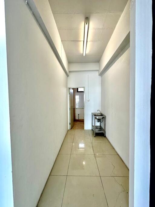 Brightly lit, narrow hallway with beige tiled flooring and a small table