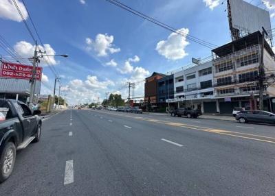 Wide asphalt road with commercial buildings on the sides under a clear blue sky