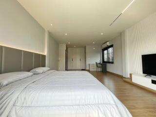 Spacious modern bedroom with a large bed, wooden flooring, and ample lighting