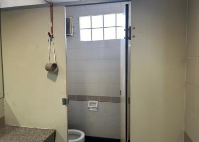 Compact bathroom with gray and white tiles, built-in toilet, small window, and partial view of the shower area