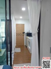 Compact interior space showing a corridor with wooden door and partial view of a kitchen, illuminated with modern downlights