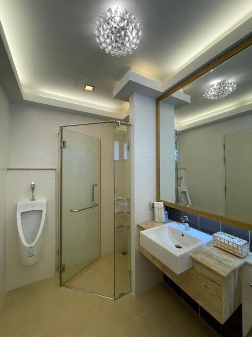 Modern bathroom with neutral tones, complete with glass shower cabin, toilet, urinal, and vanity