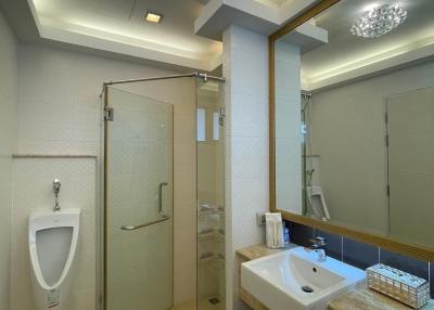 Modern bathroom with neutral tones, complete with glass shower cabin, toilet, urinal, and vanity
