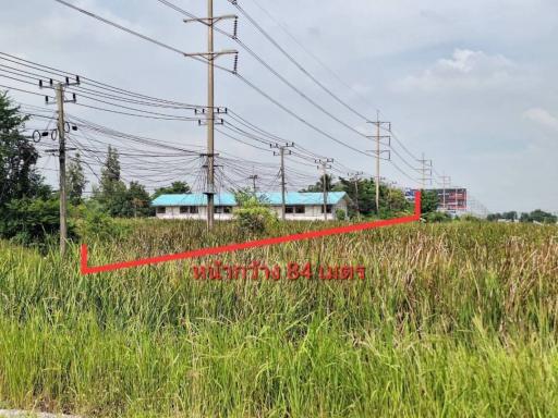 Spacious undeveloped land with utility poles and lush greenery under a cloudy sky