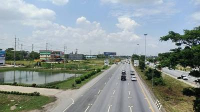 Urban road with vehicles and surrounding greenery under clear blue skies