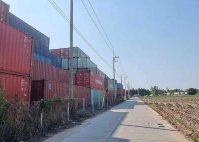 Stacked shipping containers by a paved road with fields