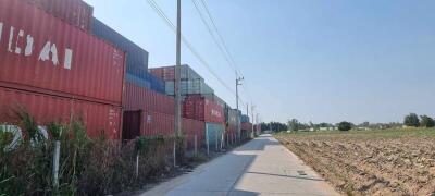 Stacked shipping containers by a paved road with fields