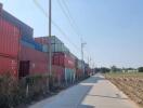 Stacked shipping containers by a paved road with fields