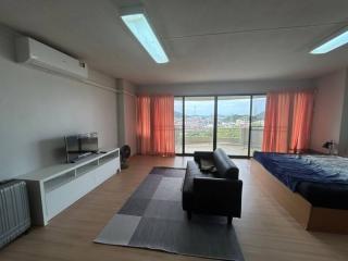 Spacious bedroom with bed, couch, television, and large window with city view