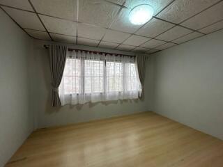 Bright and empty bedroom with large window and wooden floor