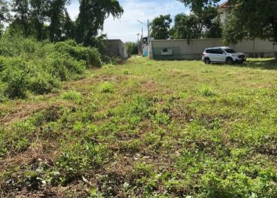 Spacious empty lot with potential for development, bordered by trees and neighboring buildings