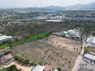 Aerial view of a large open plot of land surrounded by vegetation and buildings with mountains in the distance