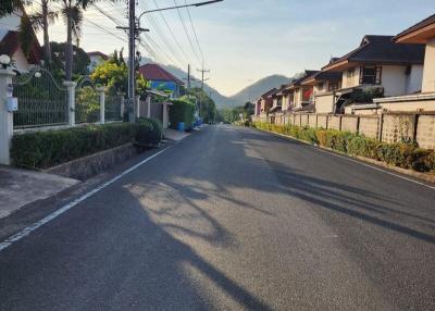 Paved residential street with houses and trees under a clear sky at sunset