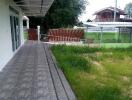 Paved walkway leading to a house with grass lawn and wooden fence