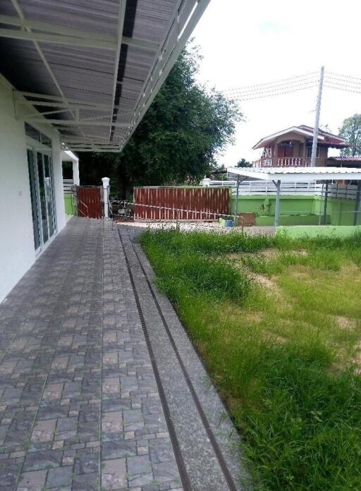 Paved walkway leading to a house with grass lawn and wooden fence