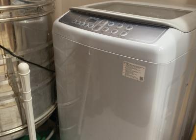 Modern top-load washing machine in a compact utility area with tiled walls