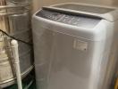 Modern top-load washing machine in a compact utility area with tiled walls