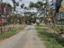 Unpaved road leading to a residential area with greenery and signage