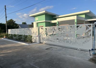 Front view of a modern green single-story house with decorative fence and paved driveway