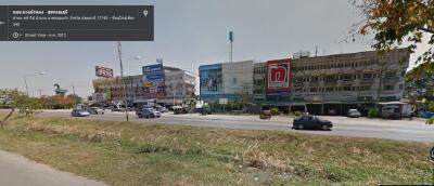 View of a commercial street with various storefronts and signage, vehicles on the road, and a visible street