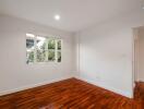 Empty bedroom with polished wooden floor and a large window